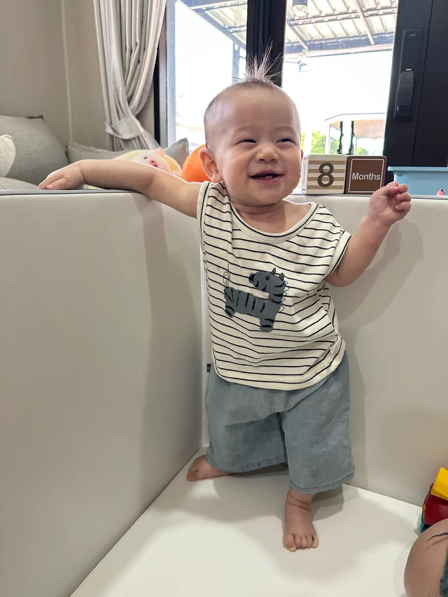 ภาพต้นฉบับ 1 — เด็กชายยืนยิ้มในคอกกั้นเด็กสีขาว ใส่เสื้อลายทาง